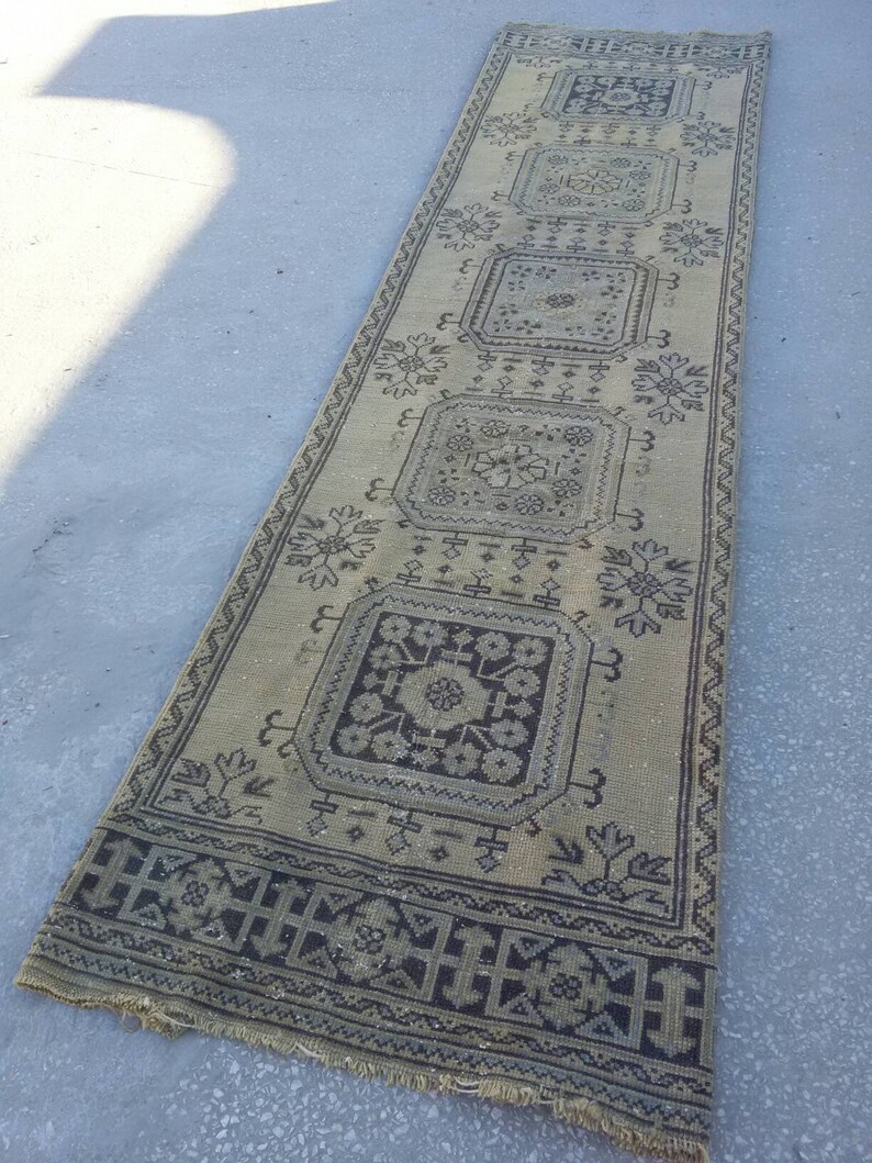 May include: A long, rectangular rug with a beige background and a black and white geometric pattern. The rug has a fringe border.
