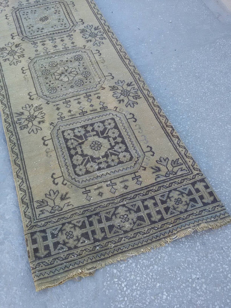 May include: A beige and brown patterned rug with a geometric design. The rug has a fringed edge and is made of a woven material.