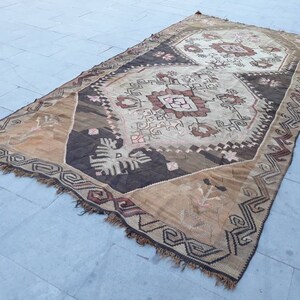 May include: A vintage Turkish rug with a brown, beige, and white geometric pattern. The rug has a fringed edge and is made of wool.