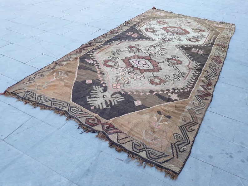May include: A vintage Turkish rug with a brown, beige, and white geometric pattern. The rug has a fringed edge and is made of wool.