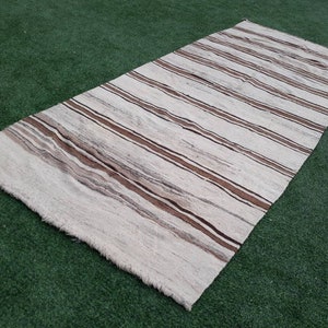 May include: A white and brown striped rug with a woven texture. The rug has a fringed edge.