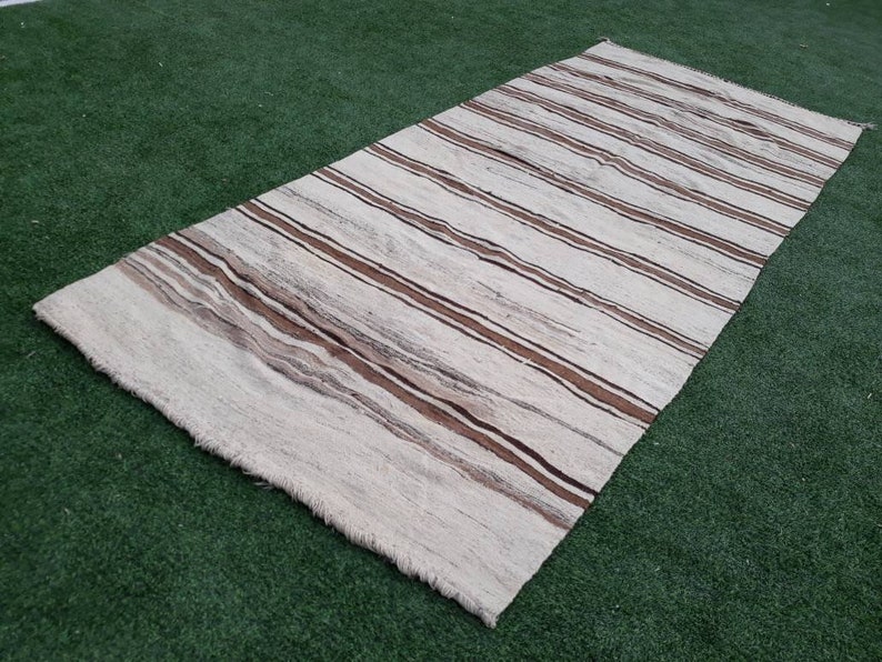May include: A white and brown striped rug with a woven texture. The rug has a fringed edge.