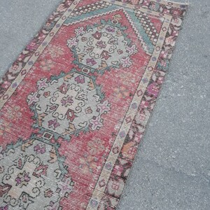 May include: A vintage Turkish runner rug with a pink, beige, and teal color scheme. The rug features a traditional geometric pattern with intricate details.