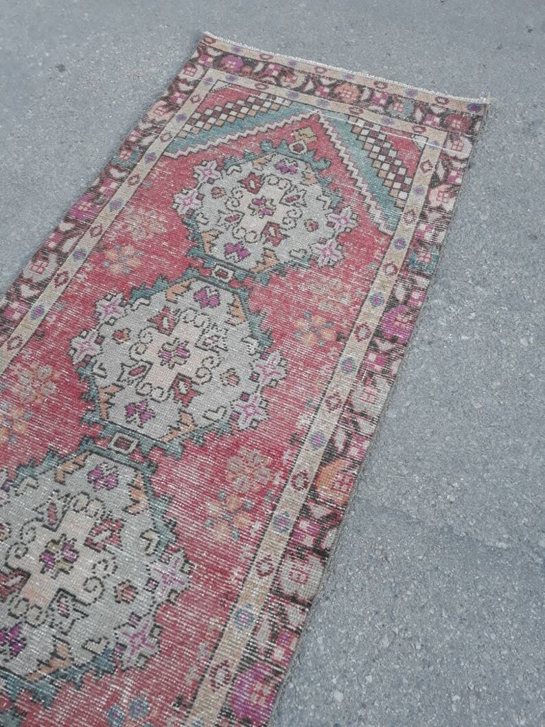 May include: A vintage Turkish runner rug with a pink, beige, and teal color scheme. The rug features a traditional geometric pattern with intricate details.