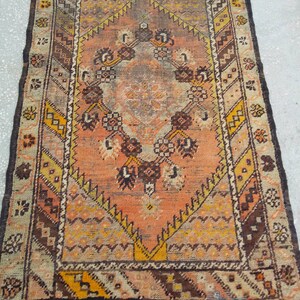 May include: A vintage rug with a geometric pattern in shades of brown, orange, and yellow. The rug has a central medallion with a floral design and a border with a repeating pattern.