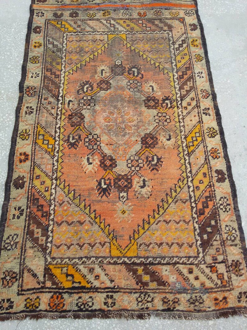 May include: A vintage rug with a geometric pattern in shades of brown, orange, and yellow. The rug has a central medallion with a floral design and a border with a repeating pattern.