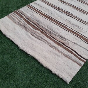 May include: A white and brown striped rug with a fringed edge. The rug is made of a soft, woven material.