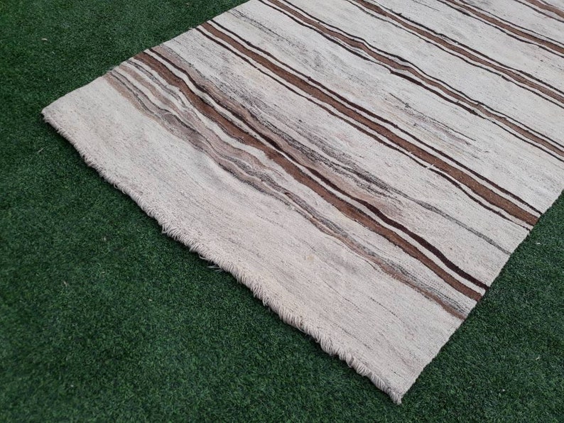 May include: A white and brown striped rug with a fringed edge. The rug is made of a soft, woven material.