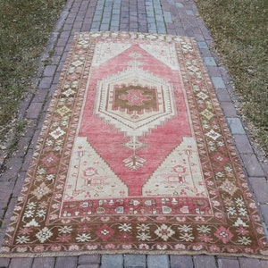 May include: A vintage Turkish rug with a pink and brown color scheme. The rug has a central medallion with a geometric design and a floral border.