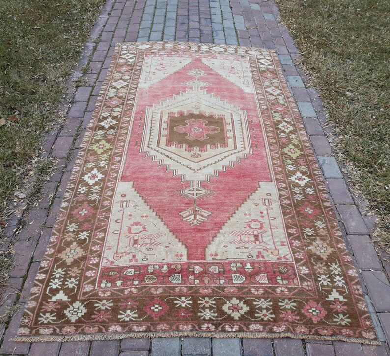 May include: A vintage Turkish rug with a pink and brown color scheme. The rug has a central medallion with a geometric design and a floral border.