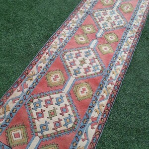 May include: A long, narrow rug with a geometric pattern in shades of red, blue, green, and white. The rug has a traditional, hand-woven look.