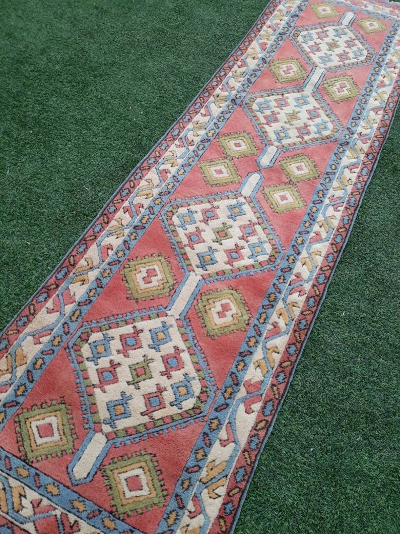 May include: A long, narrow rug with a geometric pattern in shades of red, blue, green, and white. The rug has a traditional, hand-woven look.