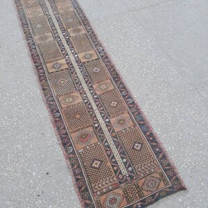 May include: A long, narrow rug with a traditional Persian design. The rug is primarily beige with brown, black, and red accents. The rug has a fringe on both ends.