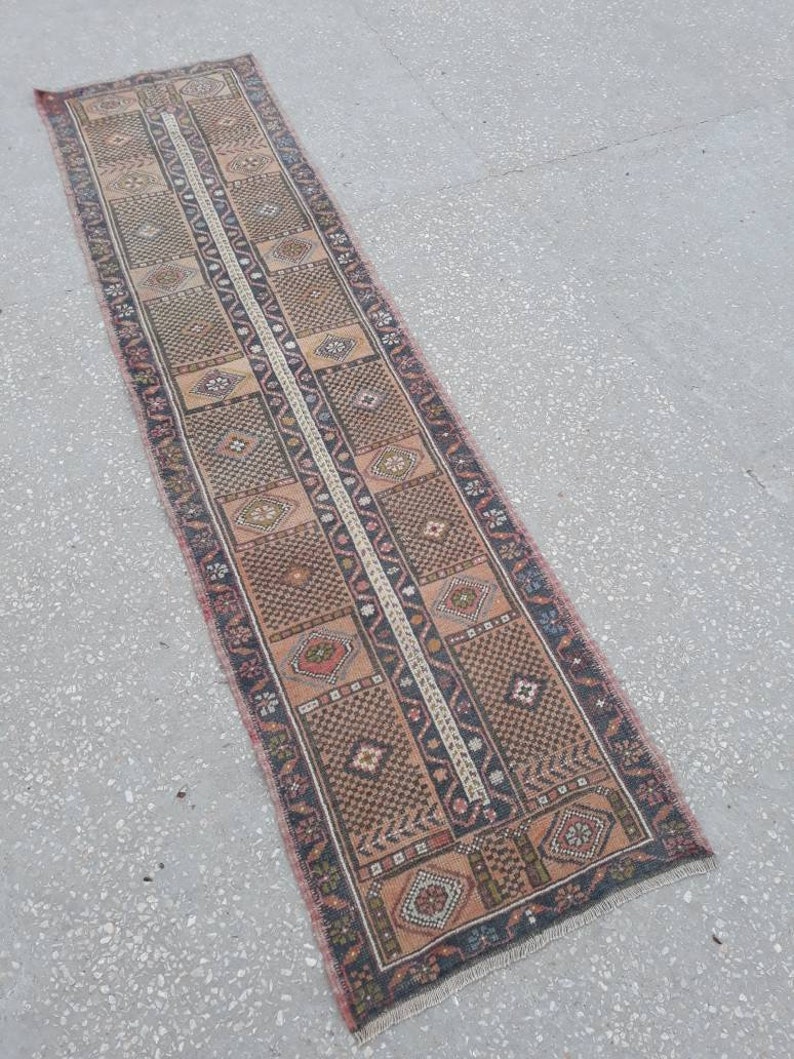 May include: A long, narrow rug with a traditional Persian design. The rug is primarily beige with brown, black, and red accents. The rug has a fringe on both ends.