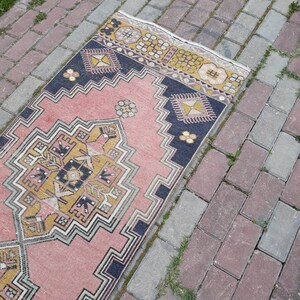 May include: A pink and yellow patterned rug with a geometric design. The rug is laid out on a brick walkway.