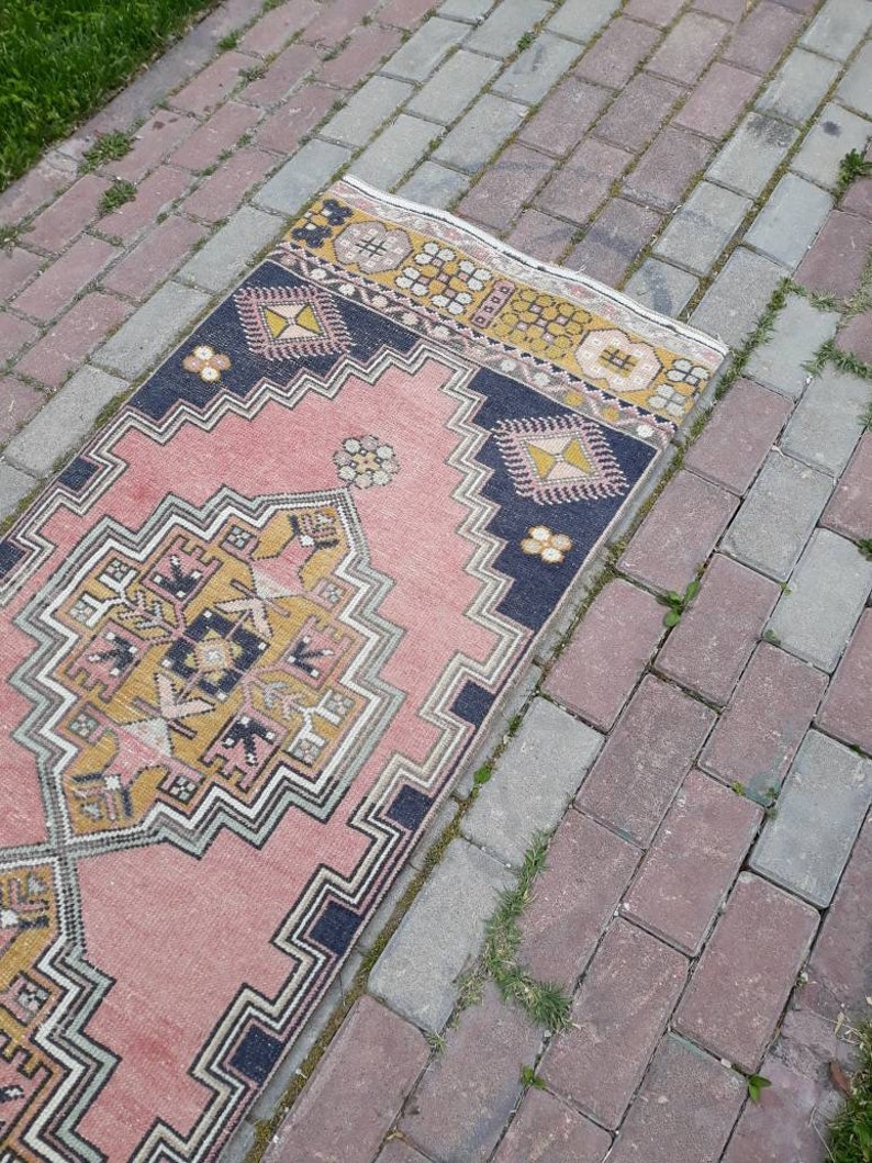 May include: A pink and yellow patterned rug with a geometric design. The rug is laid out on a brick walkway.