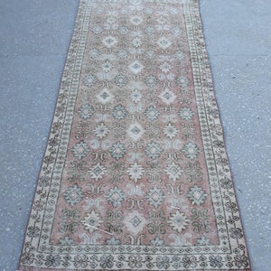 K&ouml;nnte beinhalten: Ein Vintage-L&auml;ufer mit einem geometrischen Muster in Rosa, Creme und Gr&uuml;n. Der Teppich hat einen Fransenrand und ist aus Wolle.