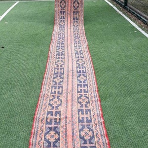 May include: A long, narrow rug with a traditional Persian design. The rug has a red border with a blue and pink center. The center of the rug features a geometric pattern.