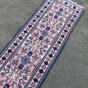 May include: A long, narrow pink and blue rug with a geometric pattern. The rug has a white background with pink and blue floral designs.