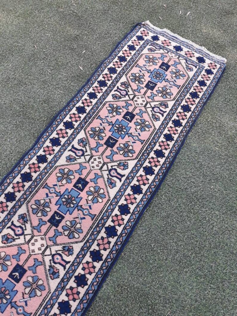 May include: A long, narrow pink and blue rug with a geometric pattern. The rug has a white background with pink and blue floral designs.