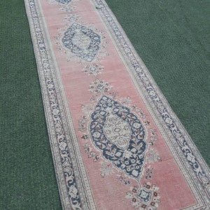 May include: A pink runner rug with a traditional floral pattern in shades of black, white, and beige. The rug has a fringed edge and is made of a soft, durable material.