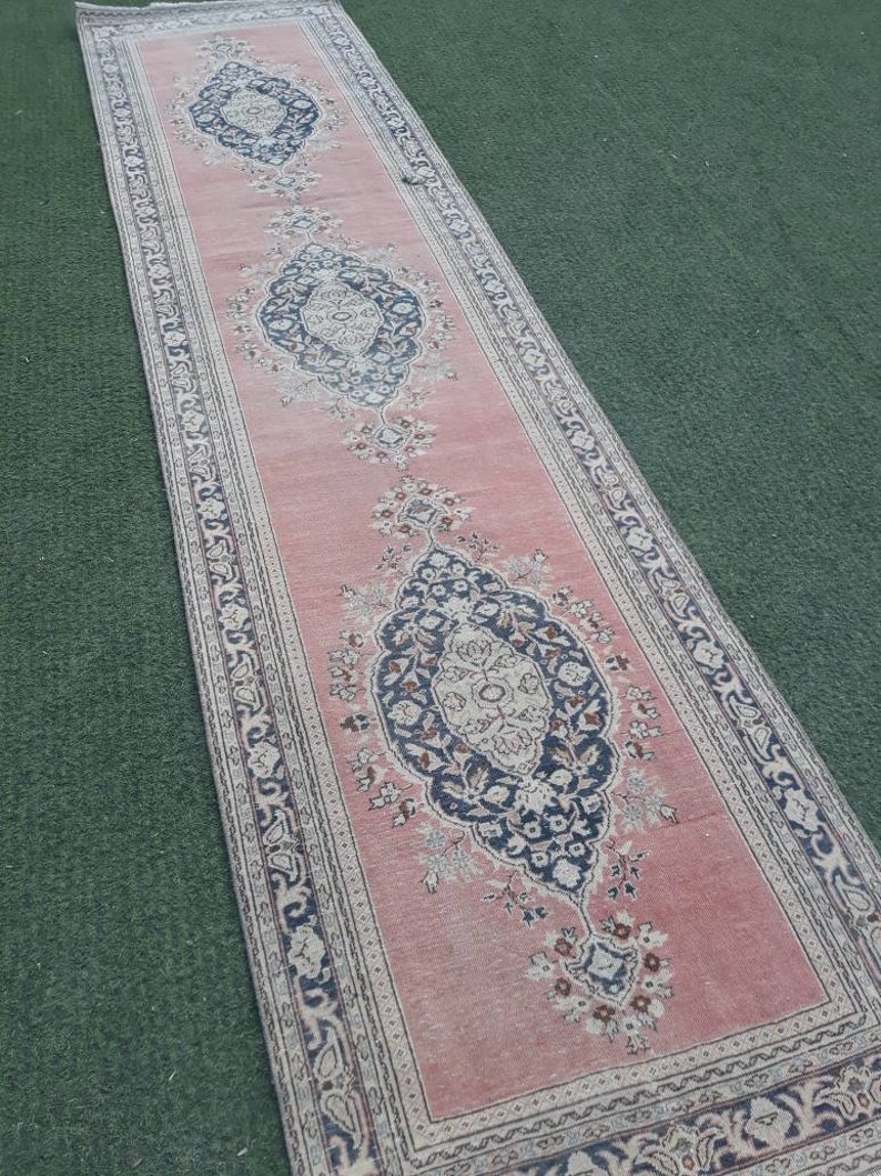 May include: A pink runner rug with a traditional floral pattern in shades of black, white, and beige. The rug has a fringed edge and is made of a soft, durable material.