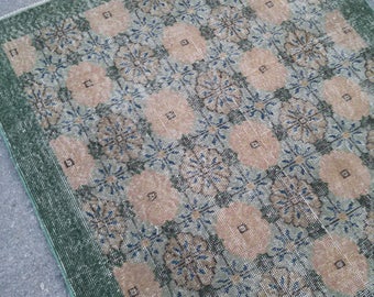 May include: A vintage rug with a geometric pattern in shades of green, beige, and blue. The rug has a distressed look, with some areas showing wear and tear.