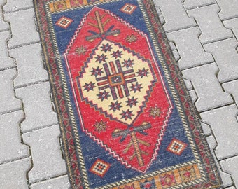 May include: A red, blue, and yellow patterned rug with a geometric design. The rug has a fringe border and is made of wool.