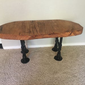 May include: A rustic wooden coffee table with a live edge top and black metal pipe legs.