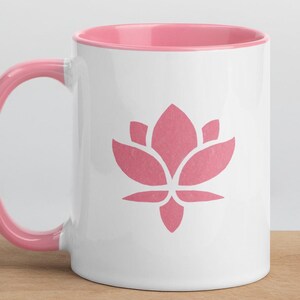 May include: A white ceramic mug with a pink interior and a pink lotus flower design. The mug is sitting on a wooden surface.