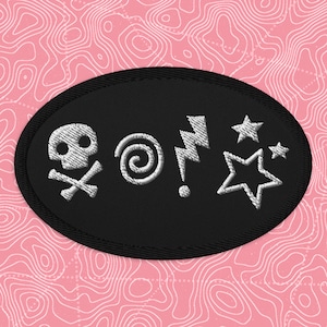 May include: Black oval patch embroidered with white skull and crossbones, swirl, lightning bolt, and stars. The patch has a black border and is set against a pink background with a white topographic pattern.