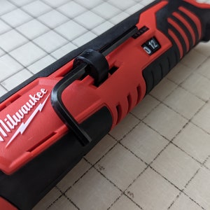 May include: A red and black Milwaukee rotary tool. The tool has a black handle with a textured grip and a red body with the Milwaukee logo in white. The tool has a black adjustment dial with the numbers 0 and 12.