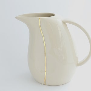 May include: A white ceramic jug with a gold stripe down the side. The jug has a wide mouth and a handle.