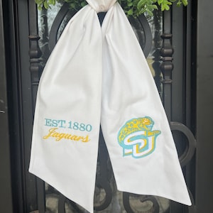 May include: White fabric scarf with the text "EST. 1880 Jaguars" embroidered in yellow on one side and a green and blue jaguar mascot with the letters "SU" embroidered on the other side.