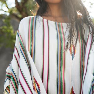 May include: A white, striped, long-sleeved shirt with colorful stripes and geometric patterns. The shirt has a relaxed fit and a round neckline.