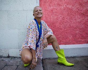 May include: A woman wearing a pink and white patterned kimono with a blue sash, crouching in front of a white and red wall. She is wearing bright yellow sparkly boots.