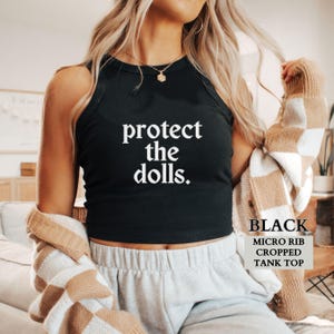 May include: Black cropped tank top with the text "protect the dolls." in white lettering.