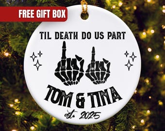 May include: White ceramic ornament with black text and graphics. The text reads "TIL DEATH DO US PART" above two skeleton hands with rings, giving the middle finger. Below, it says "TOM & TINA est. 2025". Includes a gold string for hanging.