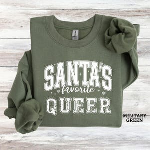 May include: A green sweatshirt with the text "Santa's favorite queer" in white lettering. The sweatshirt is a crew neck style and has a relaxed fit.