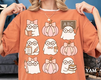 Puede incluir: Camiseta naranja con un estampado repetido de fantasmas de dibujos animados con gafas y lazos, y calabazas con lazos. Algunos fantasmas sostienen libros, un bloc de notas, una taza de café, un lápiz y una pizarra con "ABC".