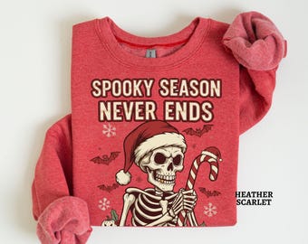 Könnte beinhalten: Heather-Scharlach-Sweatshirt mit dem Text "Spooky Season Never Ends" und einem Skelett mit Weihnachtsmütze, das eine Zuckerstange hält. Das Design umfasst Fledermäuse und Schneeflocken.