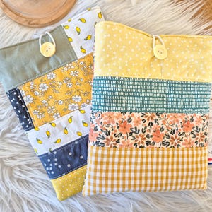 Peut inclure: Deux étuis en tissu patchwork avec fermetures à bouton. L'un présente un mélange de tissus à motifs floraux jaunes, de citrons et de motifs bleu marine. L'autre a des tissus à motifs jaunes, turquoise et floraux avec un fond vichy jaune.