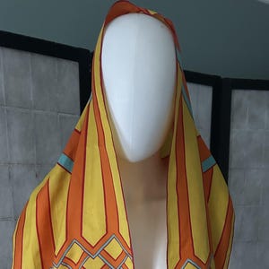 May include: A yellow, orange, and blue patterned silk scarf with a fringed edge. The scarf has a geometric design and the text "Peter Max" printed on it.