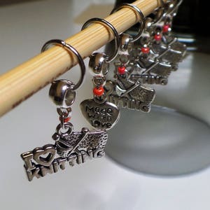 May include: Six silver knitting stitch markers with red beads. The markers feature charms with the words "I love knitting", "Made with love", and "Knitting".