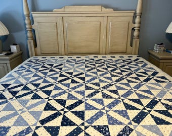 May include: A white bed frame with a blue and white patterned quilt. The headboard is made of wood and has a light brown finish.