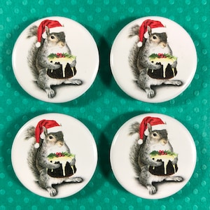May include: Four round white buttons featuring a gray squirrel wearing a Santa hat and holding a Christmas pudding. The buttons have a festive holiday theme, with a green and red holly sprig on the pudding.