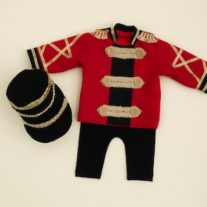 May include: A red and black costume for a baby or toddler. The costume includes a jacket with gold trim, black trousers, and a black hat with gold trim.