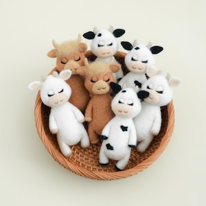 May include: A wicker basket filled with handmade felt animal toys. The toys are all white with black markings and brown accents. The toys are arranged in a circle with their heads facing the center of the basket.
