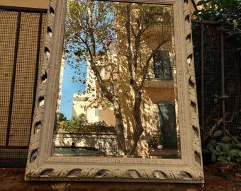May include: A white painted wooden mirror with an ornate frame. The mirror reflects a tree and a building.