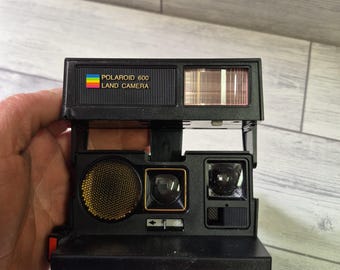 May include: A black Polaroid 660 autofocus camera with a red and gold label. The camera has a built-in flash and a viewfinder.